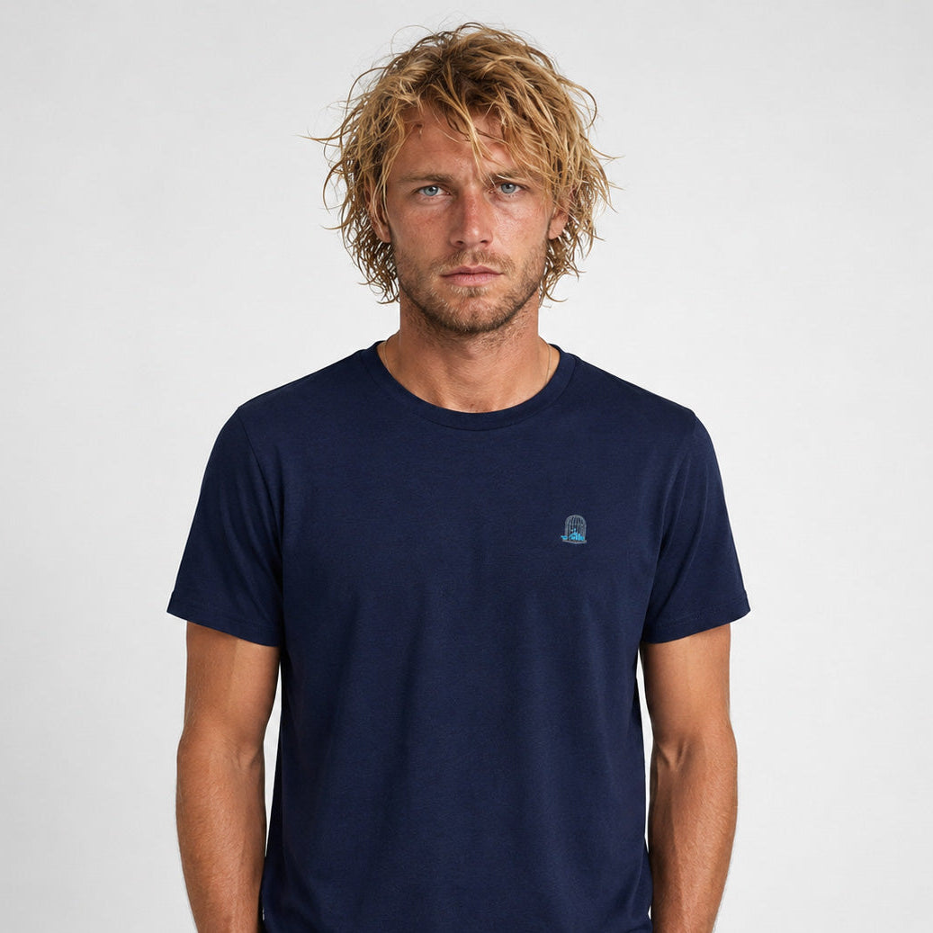 Front studio photograph of a male model wearing the Sauce & Brown Atlantic navy t-shirt with turquoise embroidered birdcage logo.