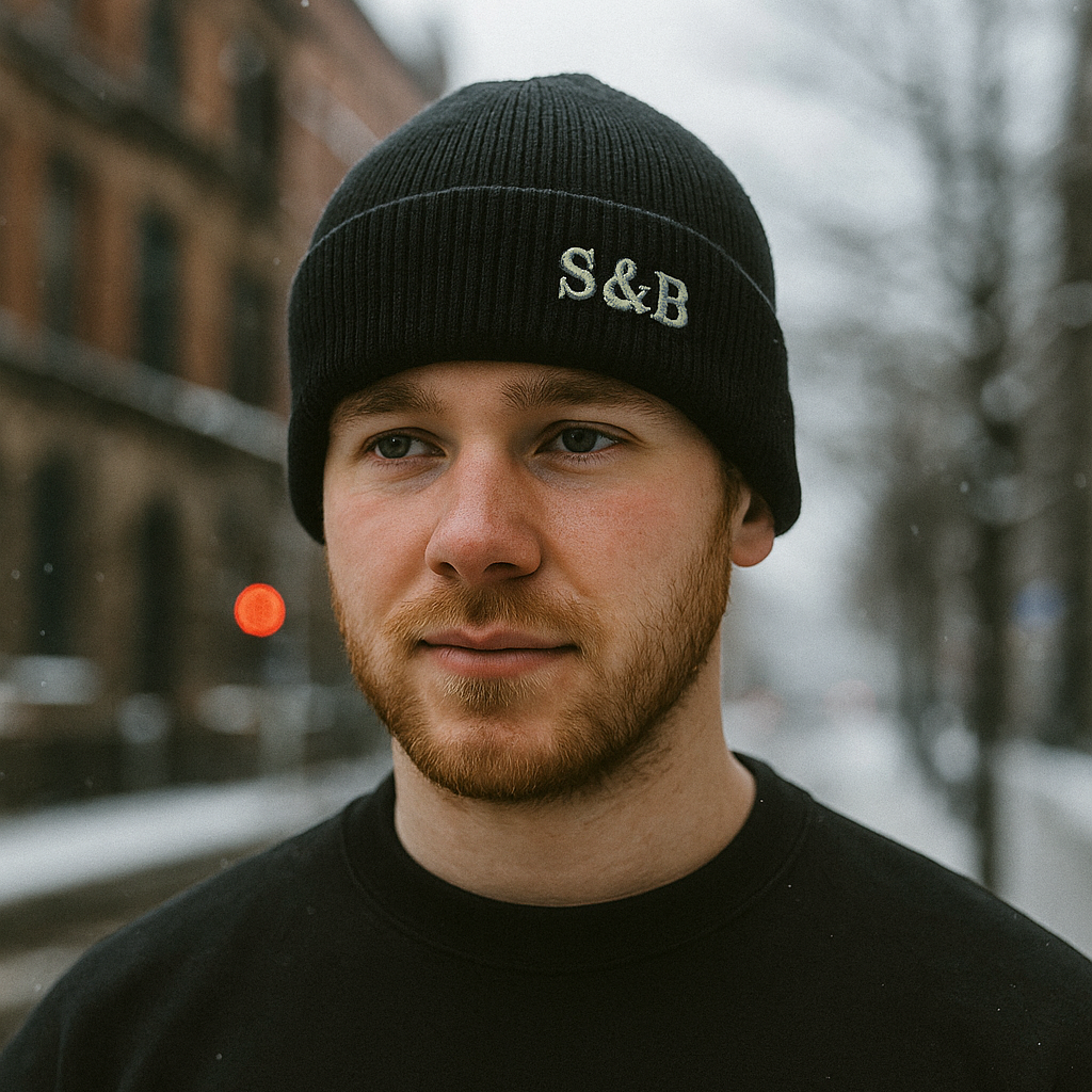 Man wearing a black beanie with 'S&B' logo outdoors on a snowy day
