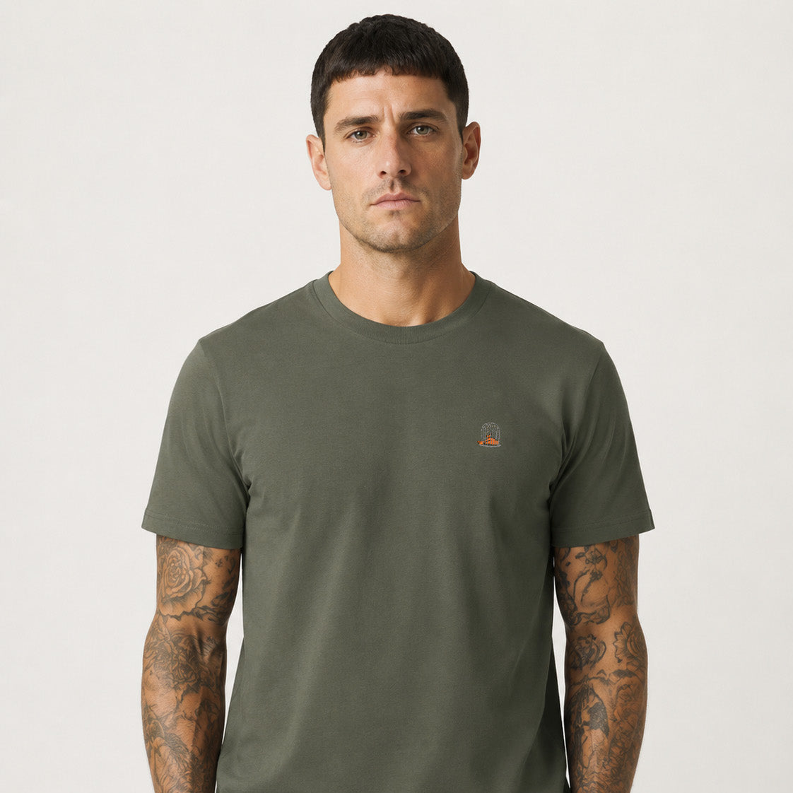 Front studio photograph of a male model wearing the Sauce & Brown Outland khaki T-Shirt with orange embroidered birdcage logo.