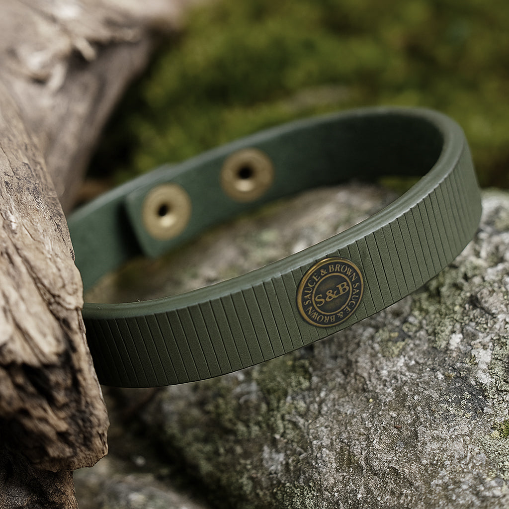 Khaki leather band with metal badge placed on natural surface by Sauce & Brown
