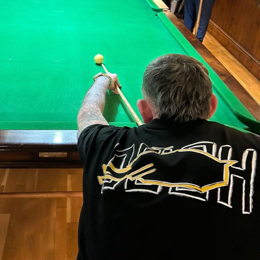 Model wearing Magnitude Box T-Shirt in black with yellow back print playing pool by Sauce & Brown