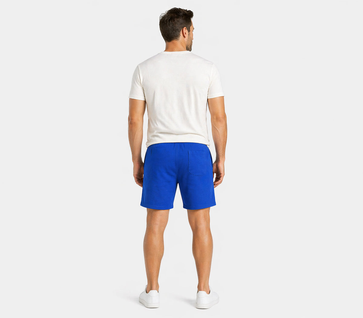 Rear view of male model wearing blue shorts with elastic waistband and white T-shirt, studio lifestyle image