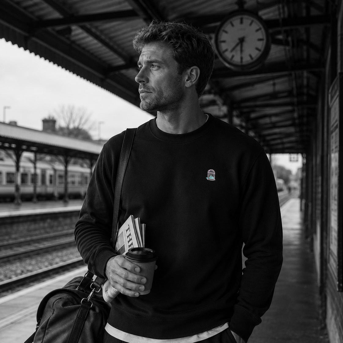 Lifestyle image of a man wearing the black Eclipse sweatshirt at a railway platform with an understated travel aesthetic