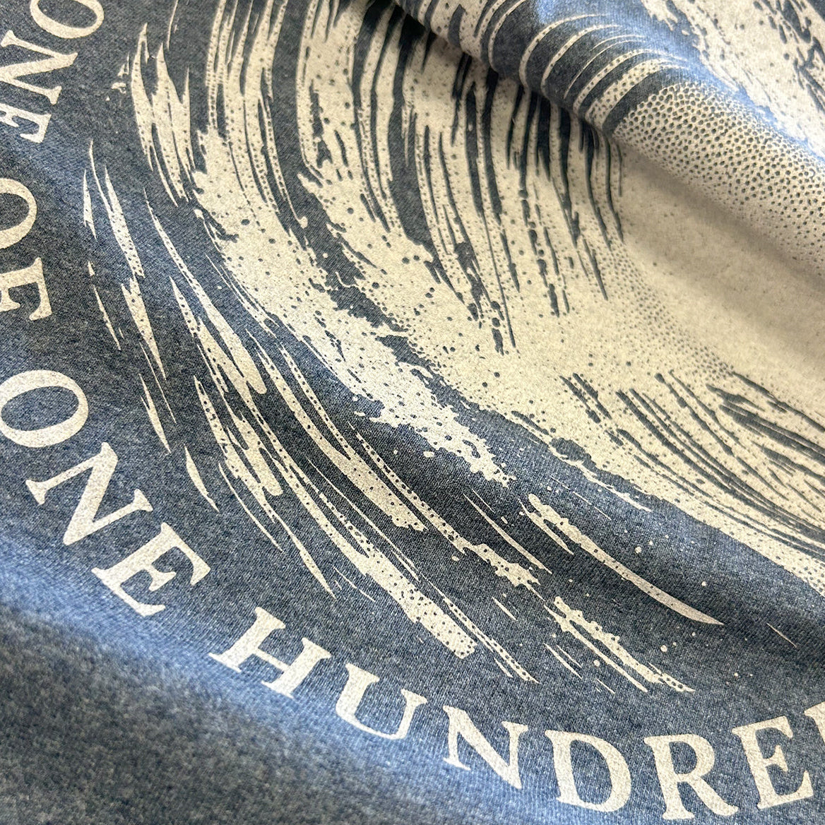 Close-up of the Evelyn Heather Navy T-Shirt showing the cream One of One Hundred wave print detail.