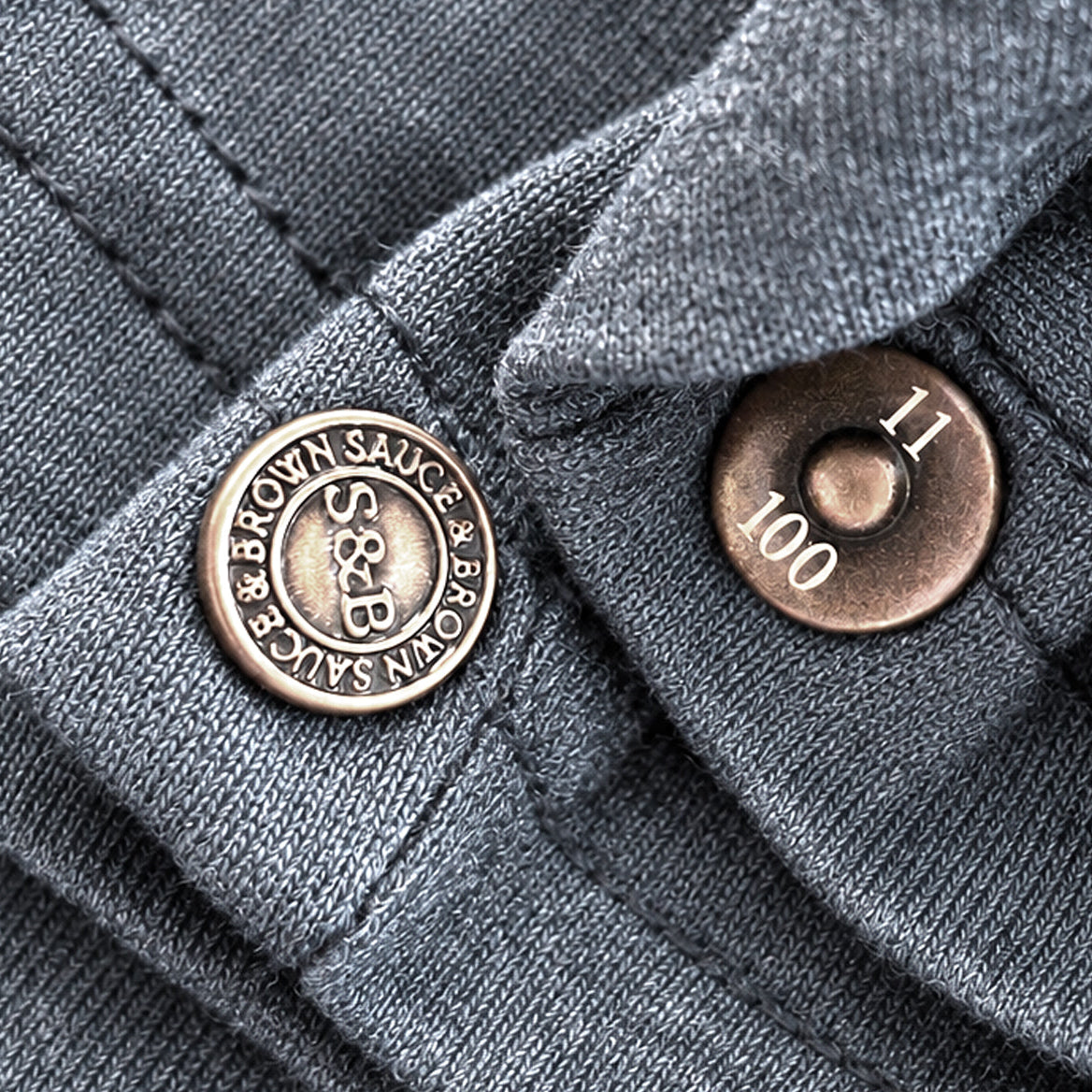 Sauce & Brown One of One Hundred numbered rivet on the Evelyn Heather Navy T-Shirt, showing 11 of 100.