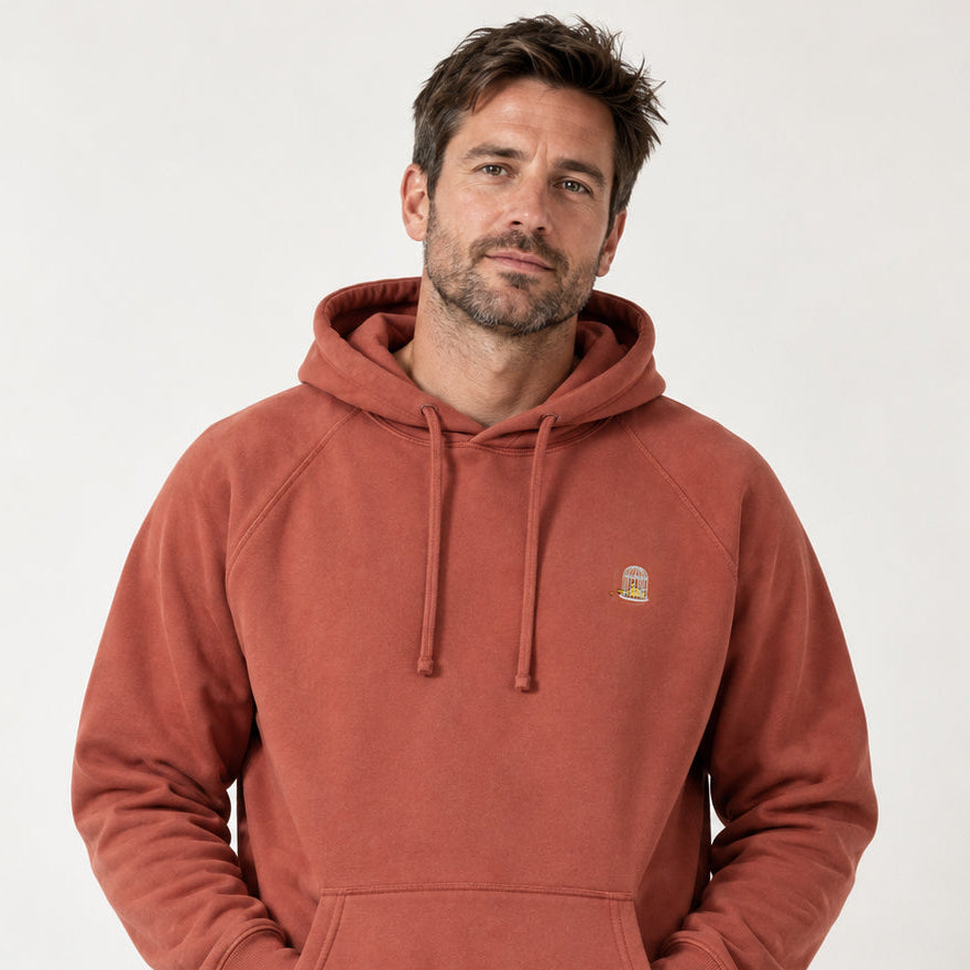 Man wearing the Sauce & Brown Kiln Hoody in Vintage Washed Terracotta. Front studio view showing the embroidered birdcage logo, raglan sleeves and relaxed fit.