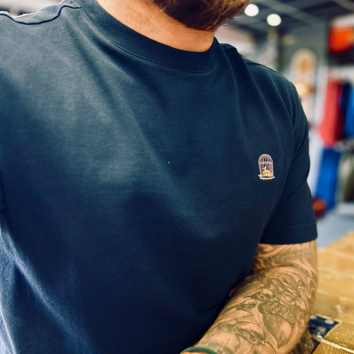 Person wearing a navy blue t-shirt with a logo, sitting at a table in an indoor setting.