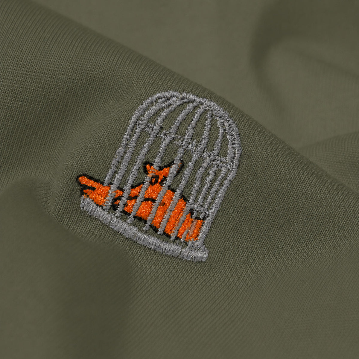 Close-up of the embroidered birdcage logo on the Sauce & Brown Outland khaki T-Shirt.
