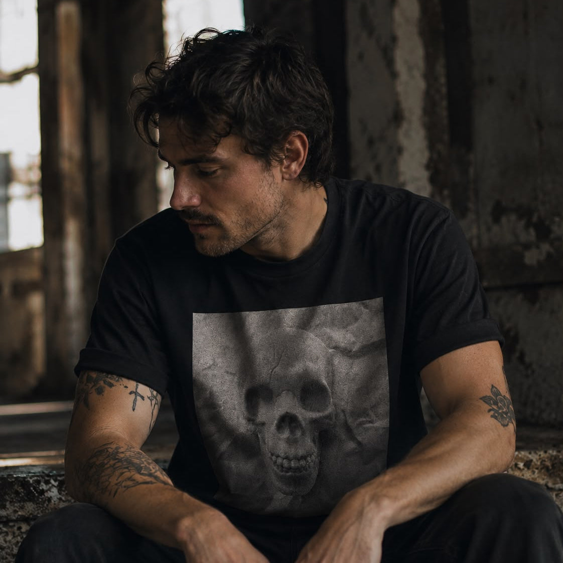 Male model wearing the Sauce & Brown Relic black T-shirt with grayscale skull graphic in a dark industrial setting.