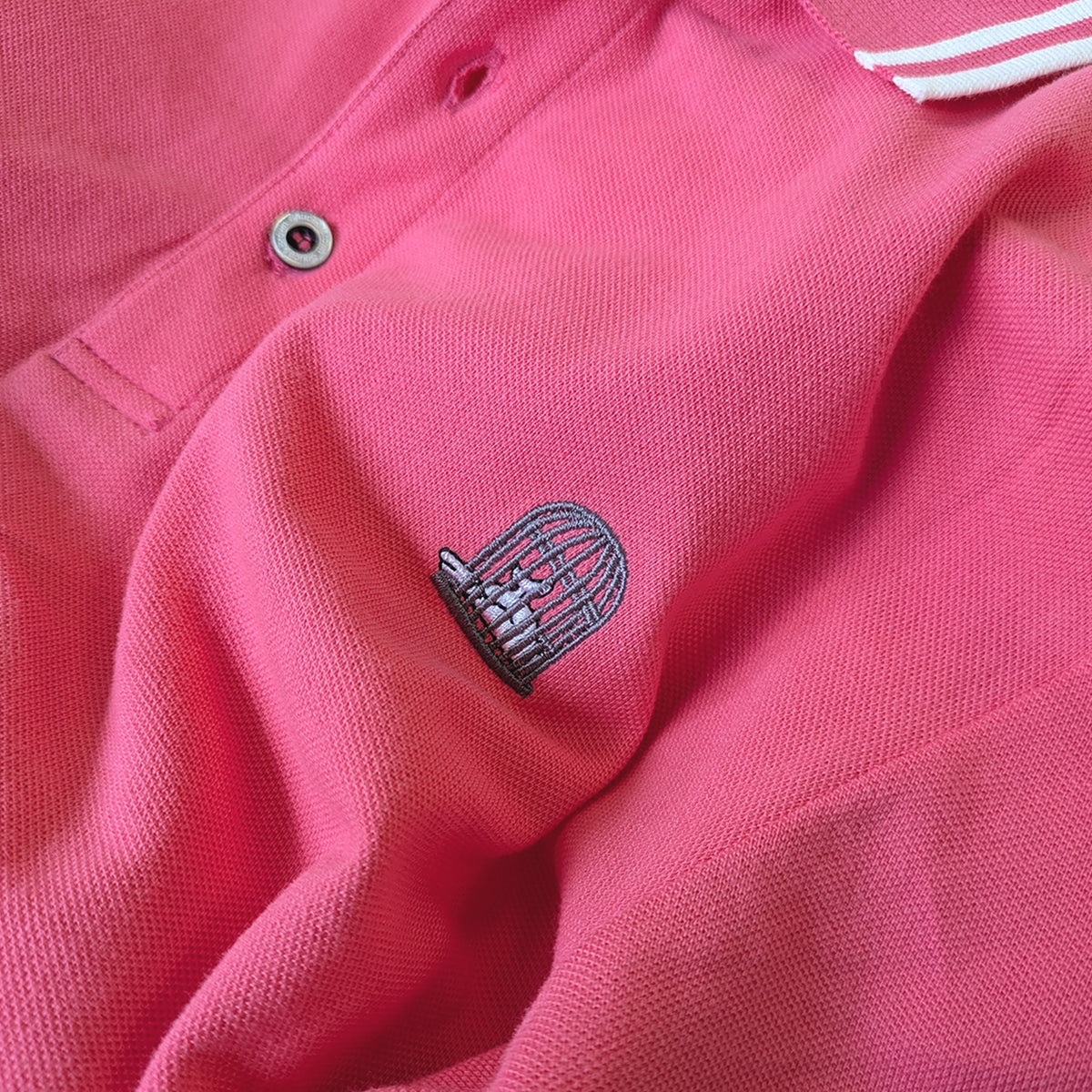 Close-up embroidered logo detail on Axel Polo in pink by Sauce & Brown