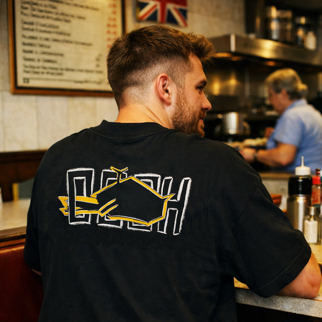 Model wearing Magnitude Box T-Shirt in black with yellow back print indoors by Sauce & Brown