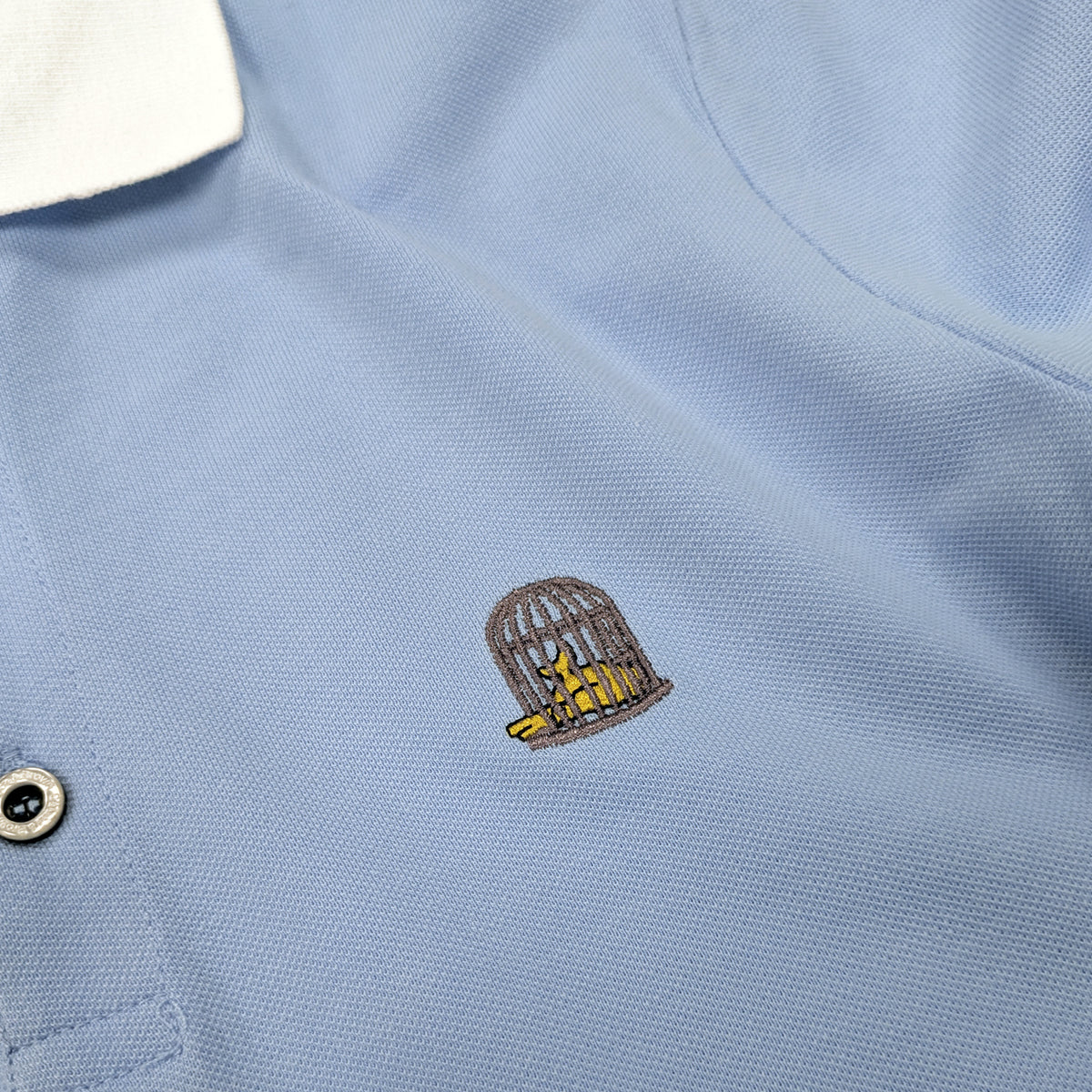 Close-up embroidered logo detail on Sola Polo in sky blue by Sauce & Brown