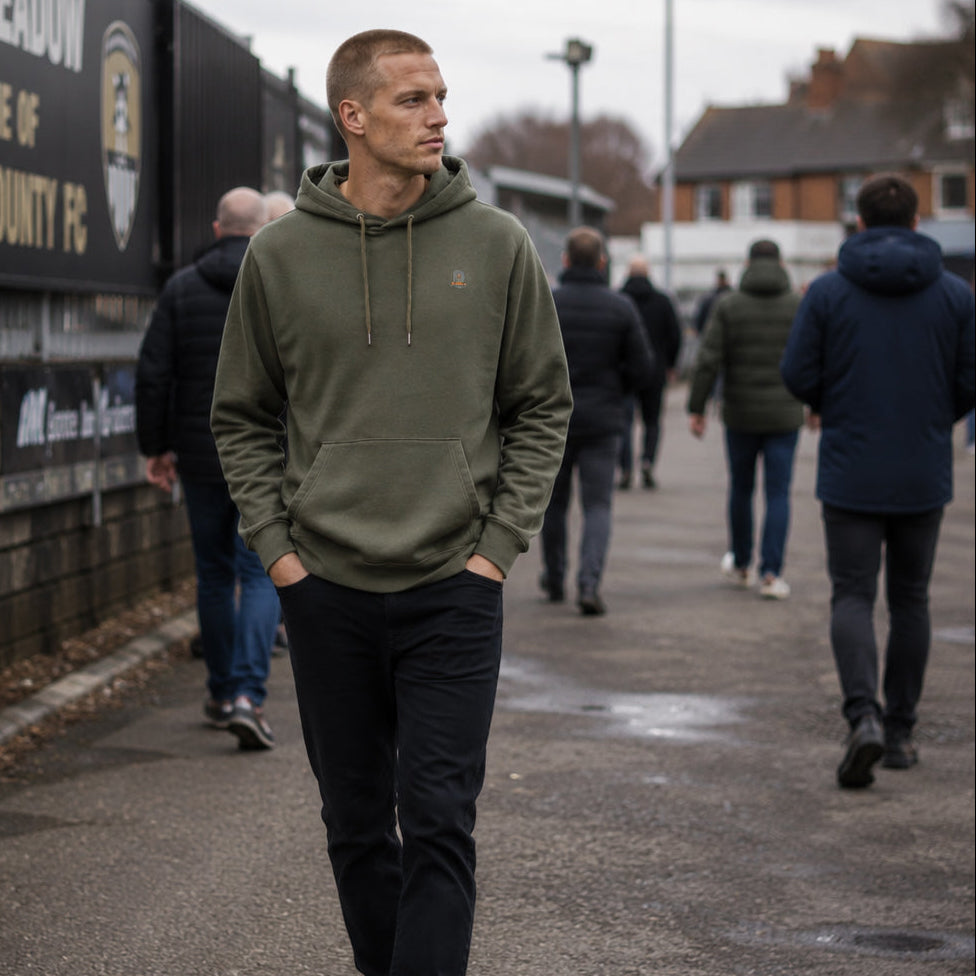 Man wearing the khaki green Tarn hoodie by Sauce & Brown walking through a town centre.