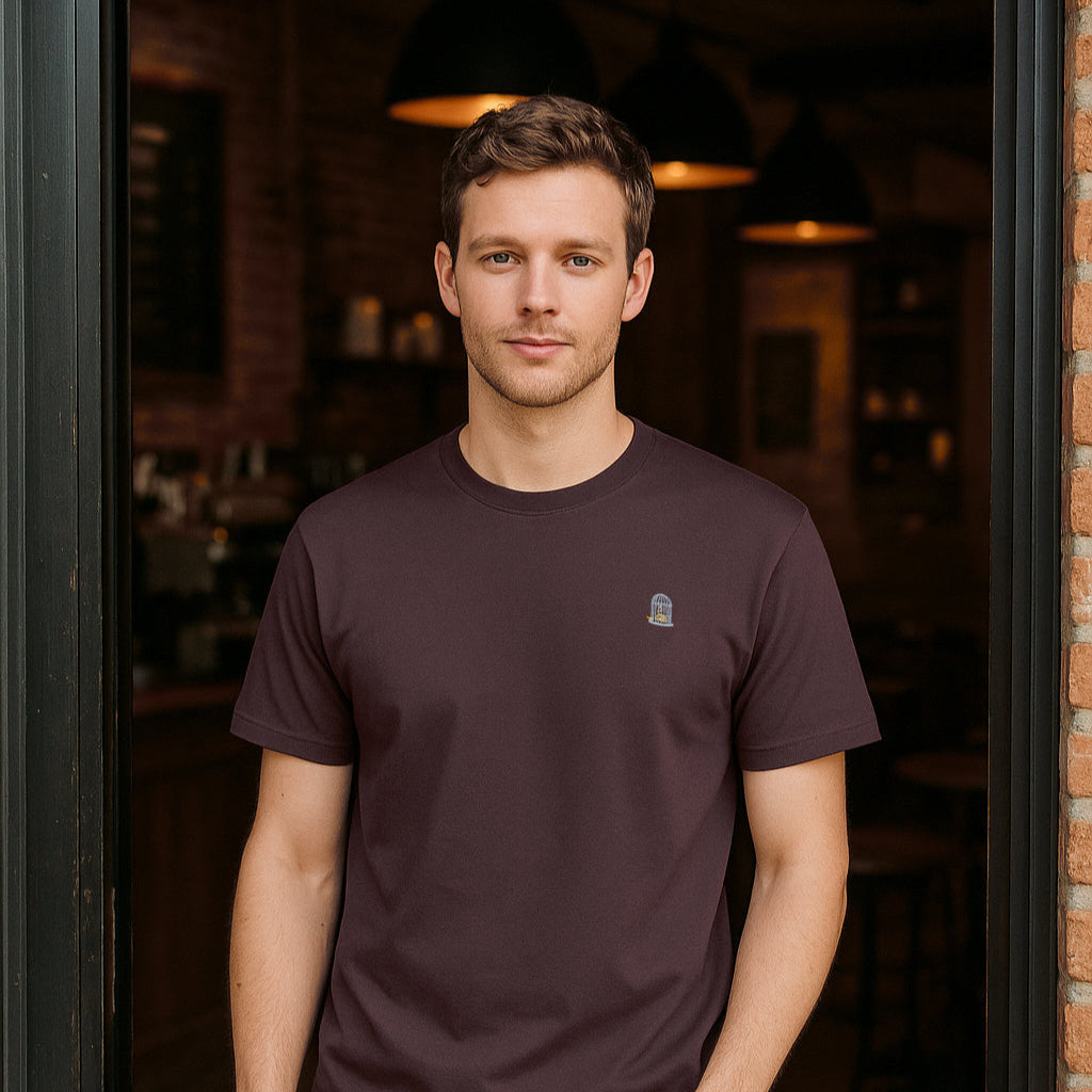 Man wearing a dark t-shirt with a small logo, standing in a dimly lit room.