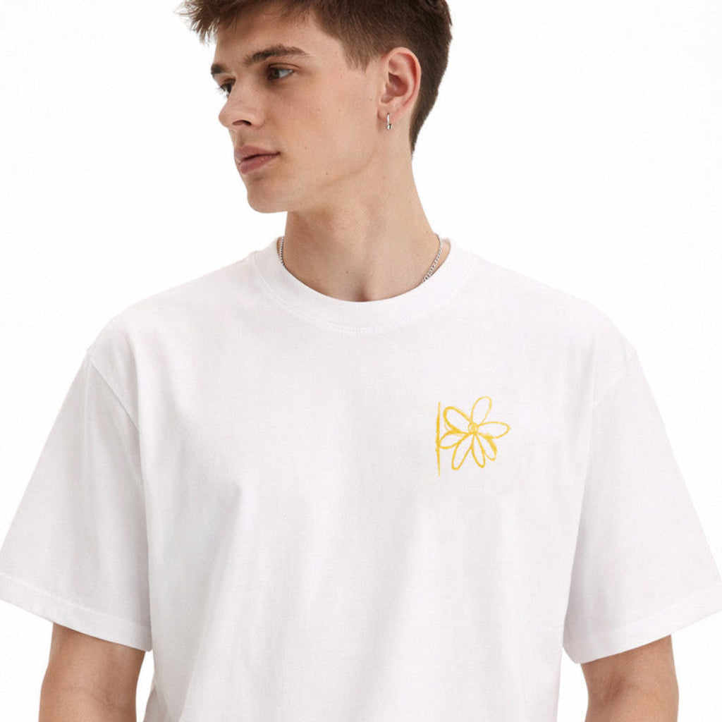 White T-shirt with yellow flower graphic worn by male model on plain studio background