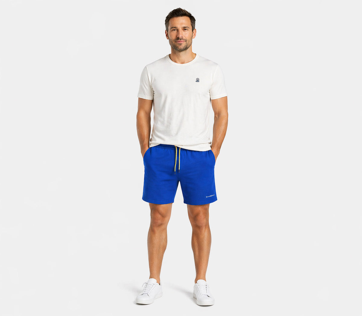 Male model wearing blue shorts with yellow drawstring and white T-shirt, full body studio lifestyle image